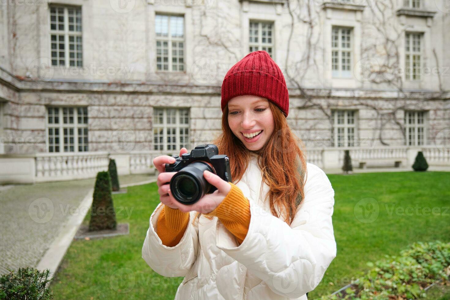 Happy redhead girl tourist, takes photos, photographer with professional camera walks around city and captures beautiful pictures photo