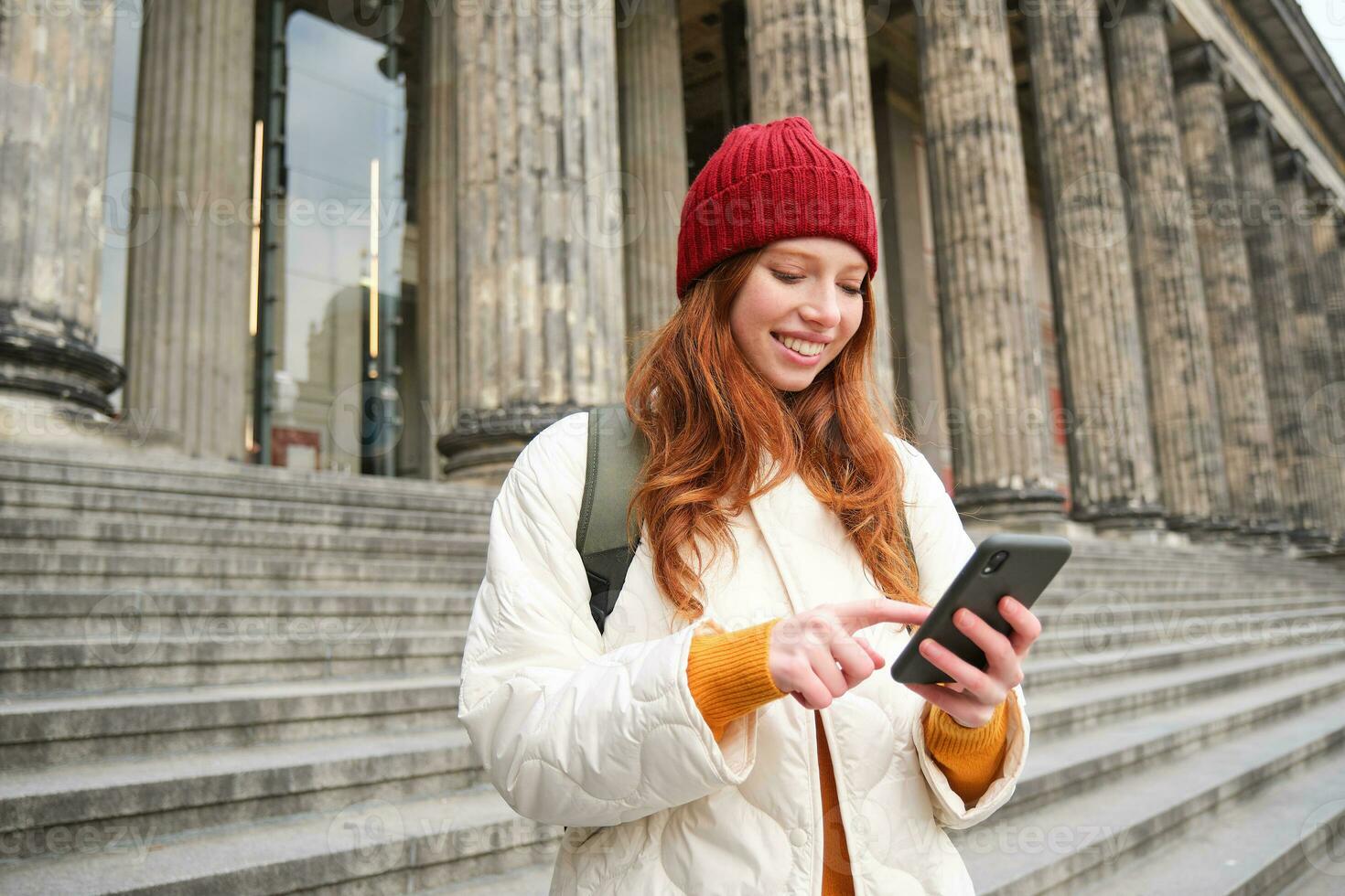 Portrait of young urban girl with backpack, using smartphone, walking around city, looking at map on mobile app, checking direction photo