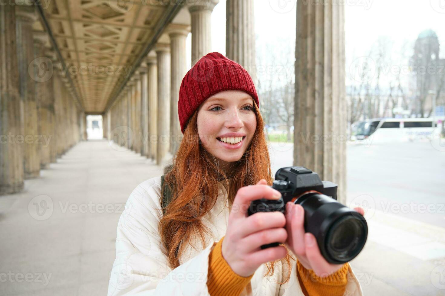 joven pelirrojo hembra fotógrafo, hace estilo de vida disparo en ciudad centro, toma fotos y sonrisas, mira para Perfecto disparo, hace imagen