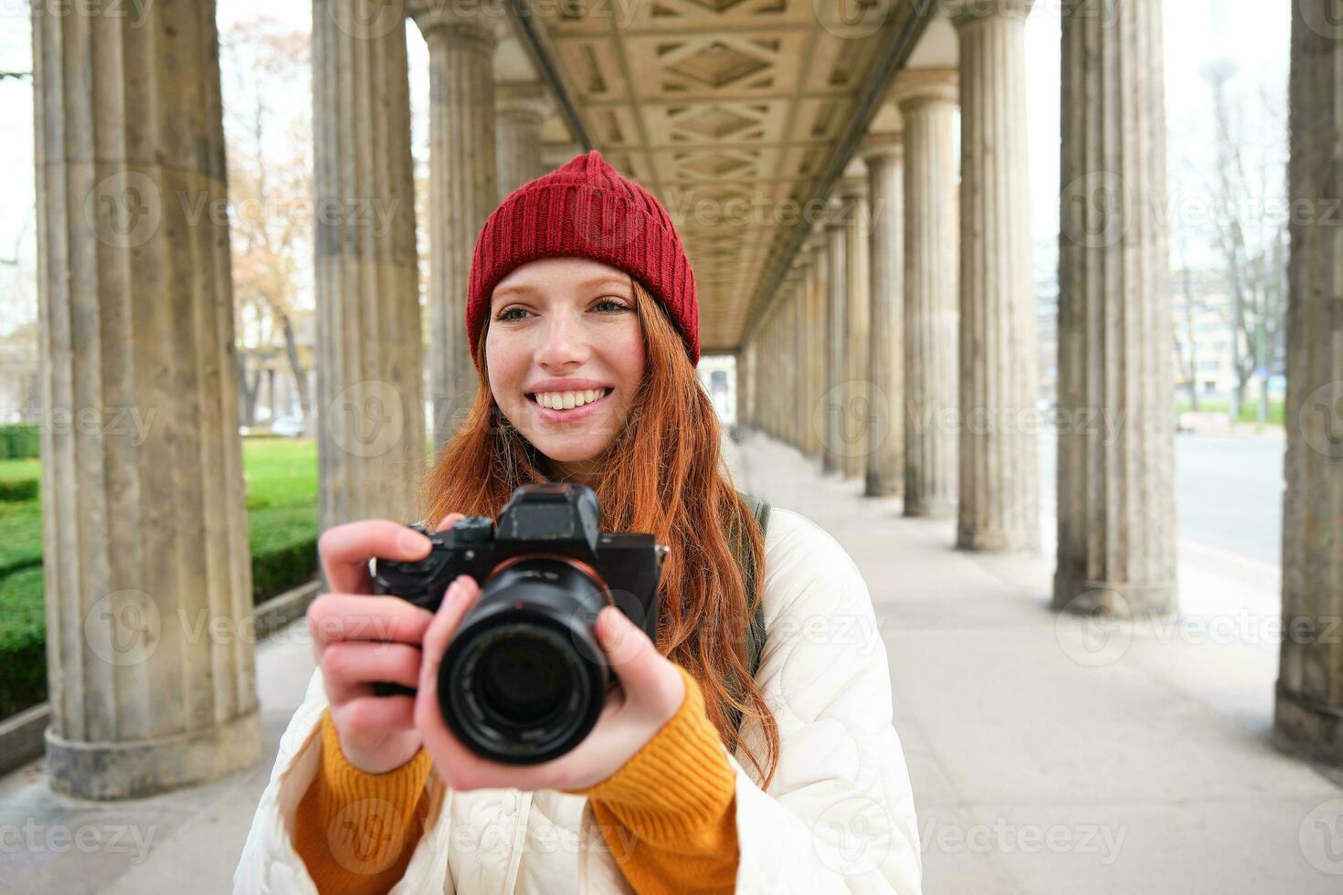 Smiling tourist photographer, takes picture during her trip, holds professional camera and makes photos