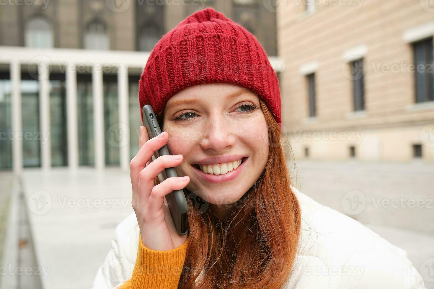 móvil conexión y personas concepto. contento pelirrojo mujer en sombrero, negociaciones en móvil teléfono, haciendo teléfono llamar, utilizando aplicación a llamada extranjero foto