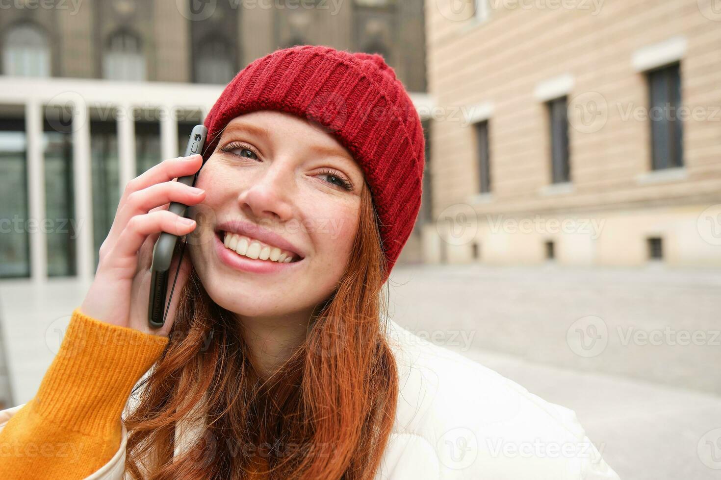 móvil conexión y personas concepto. contento pelirrojo mujer en sombrero, negociaciones en móvil teléfono, haciendo teléfono llamar, utilizando aplicación a llamada extranjero foto