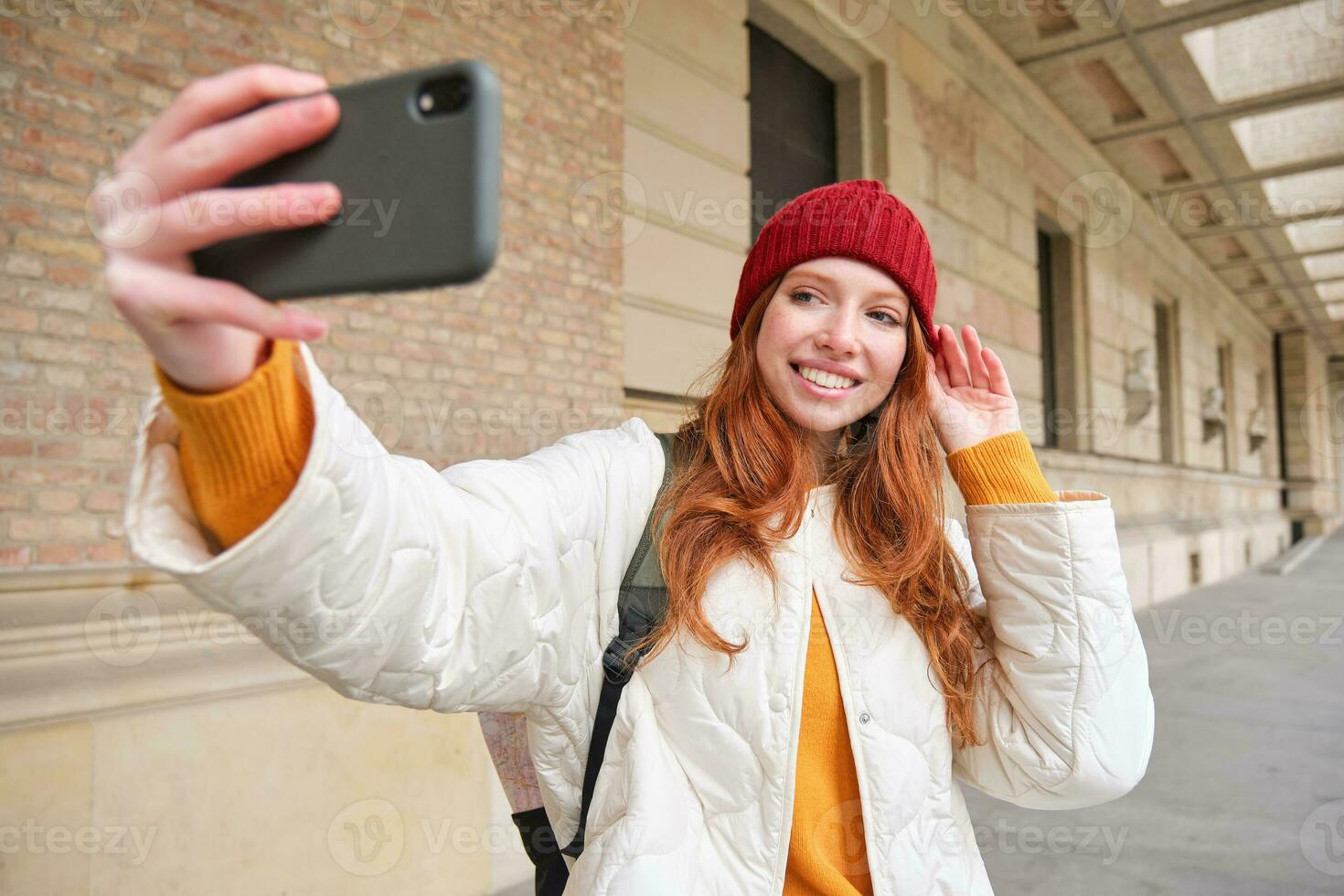 elegante pelirrojo niña turista, toma selfie en frente de turismo atracción, hace foto con teléfono inteligente, mira a móvil cámara y poses