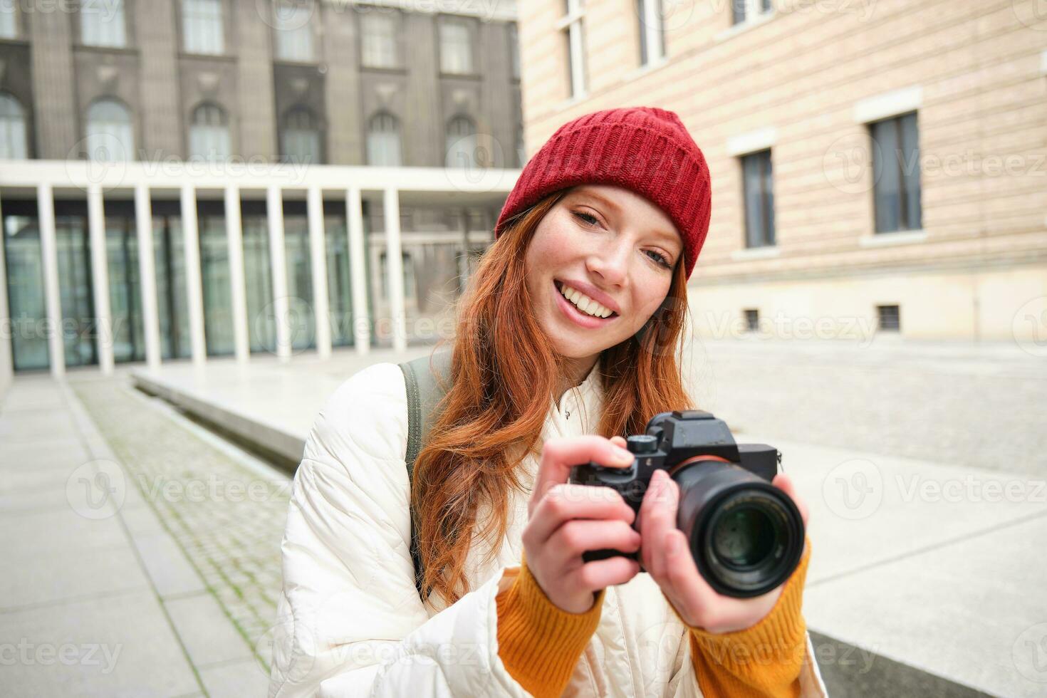 Beautiful readhead girl, photographer with professional camera takes pictures outdoors, walking around city and taking photos, sightseeing photo