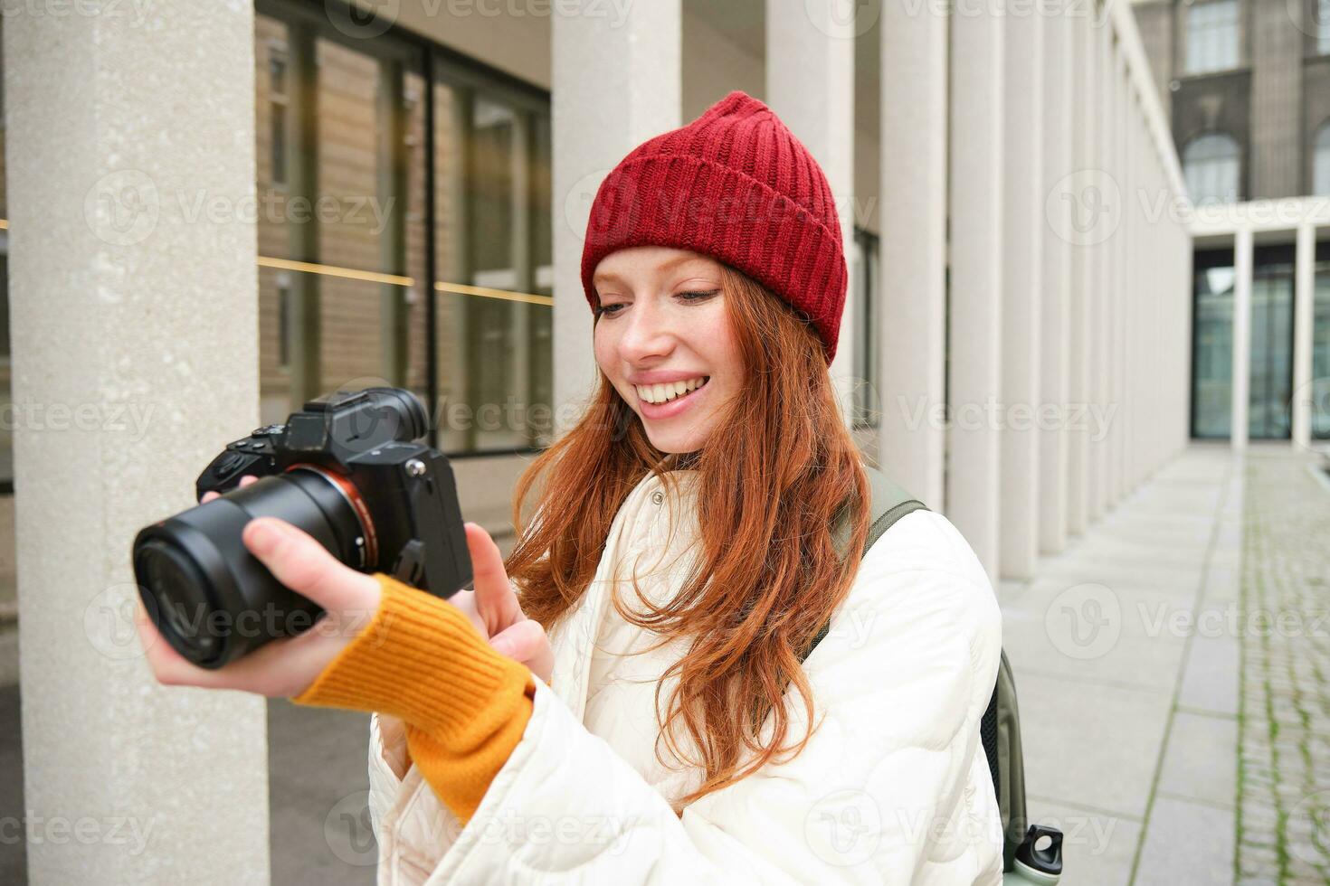 Beautiful readhead girl, photographer with professional camera takes pictures outdoors, walking around city and taking photos, sightseeing photo