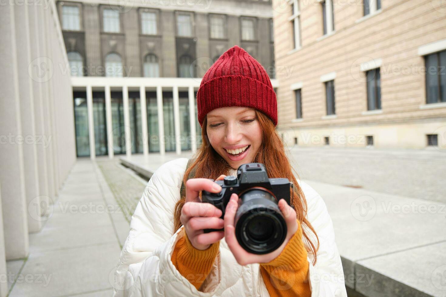 sonriente pelirrojo niña fotógrafo, tomando imágenes en ciudad, hace fotos al aire libre en profesional cámara