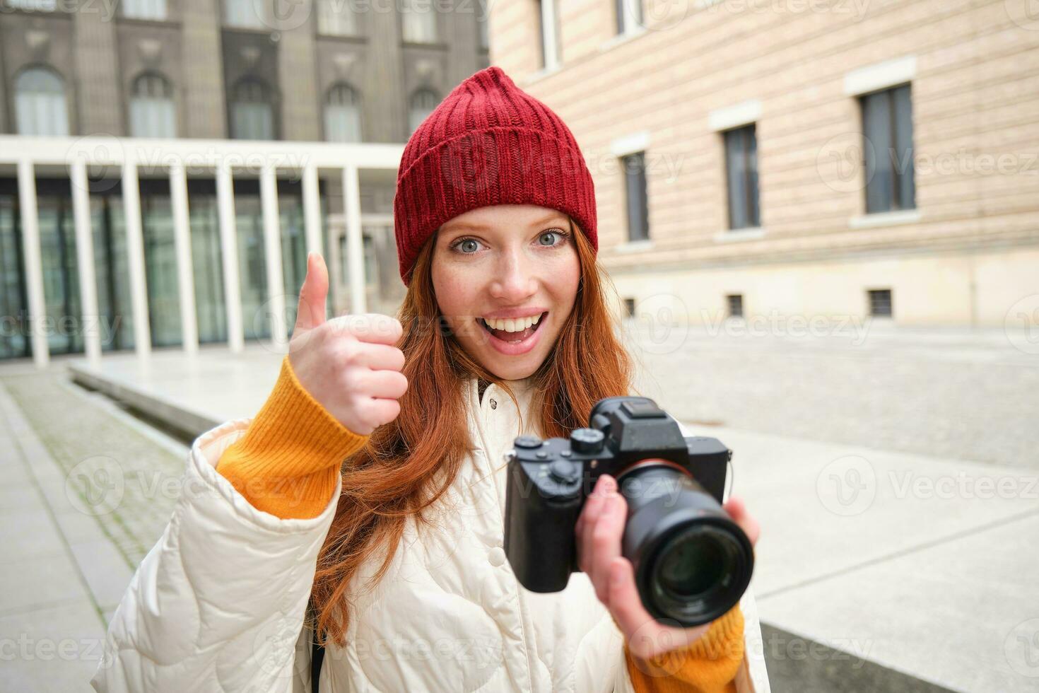 Beautiful readhead girl, photographer with professional camera takes pictures outdoors, walking around city and taking photos, sightseeing photo