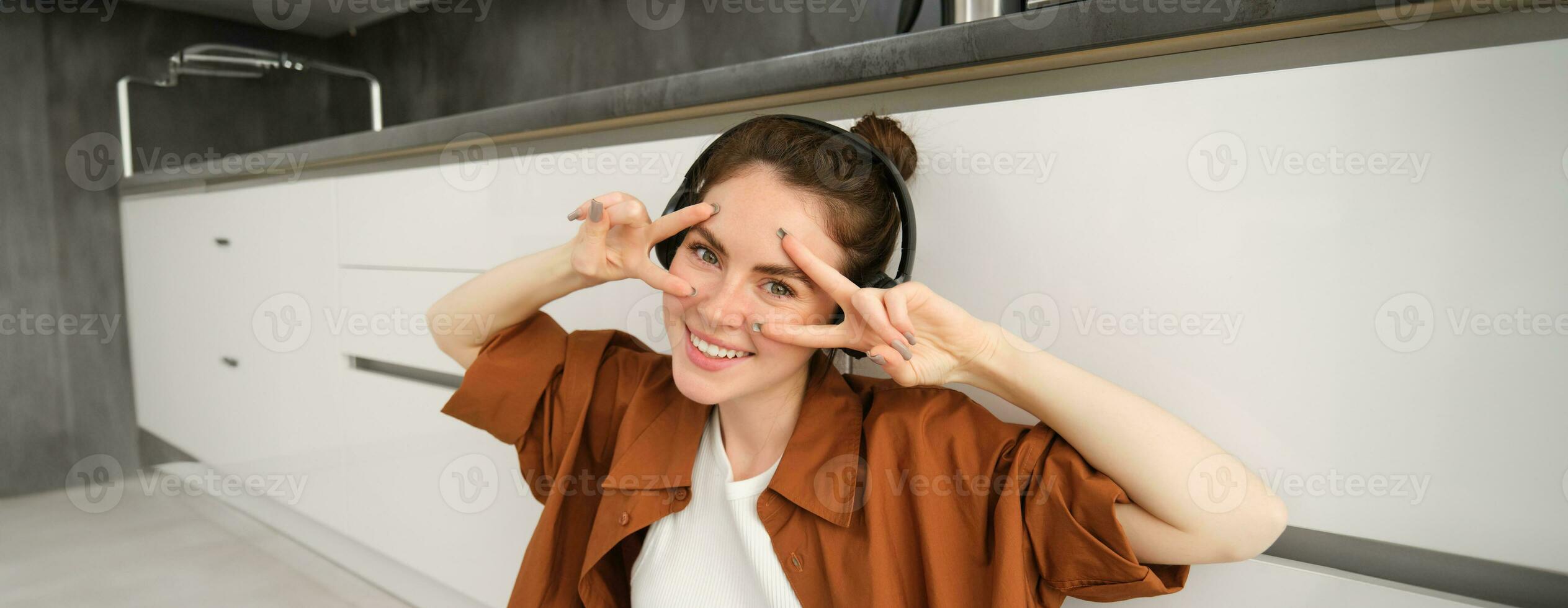 Happy young woman in headphones, listens music, enjoys sound quality, shows vsign photo