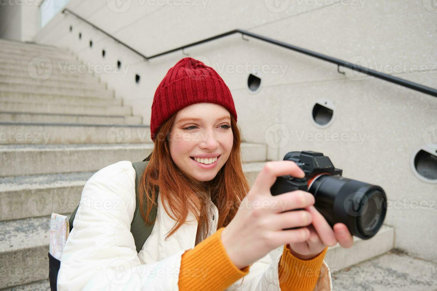 urbano personas y estilo de vida. contento pelirrojo mujer toma fotos, participación profesional digital cámara, fotografiando en calles foto