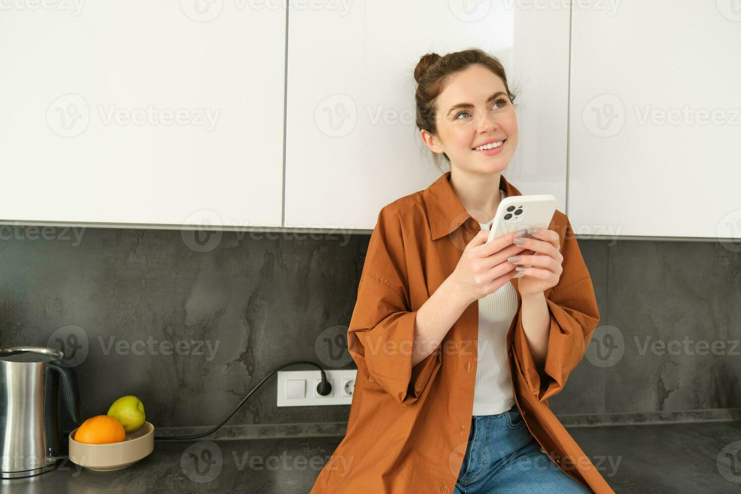 Image of young woman with smartphone, looking with thoughtful expression, buying online using mobile app, orders food delivery with phone application photo