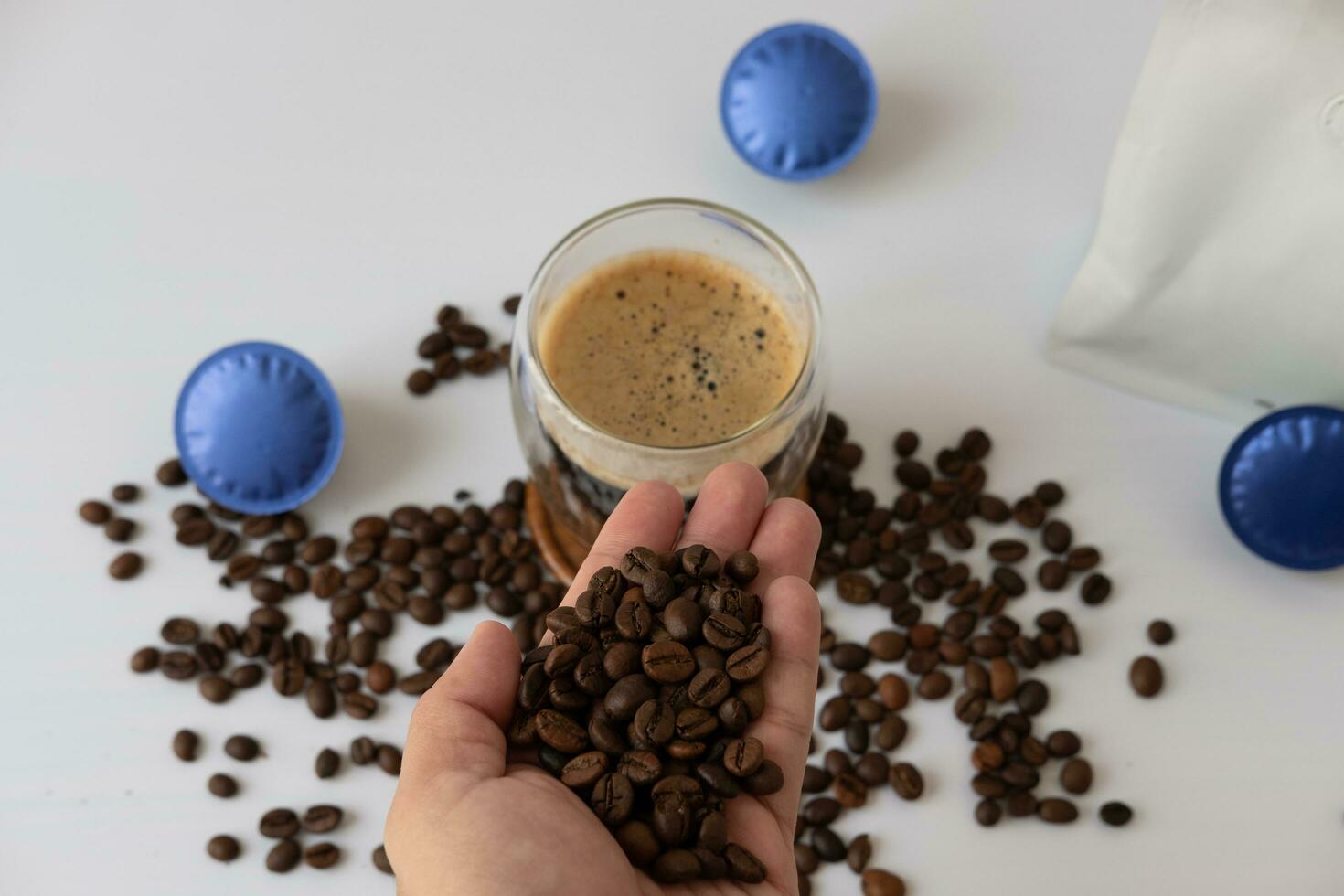 Male hand holding coffee beans Coffee mug with crema With coffee capsule elements on a white background photo