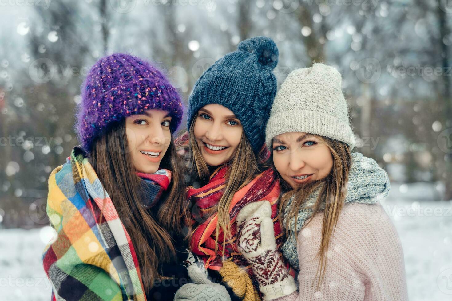 Three women friends outdoors in knitted hats having fun on a snowy cold weather. Group of young female friends outdoors in winter park. photo