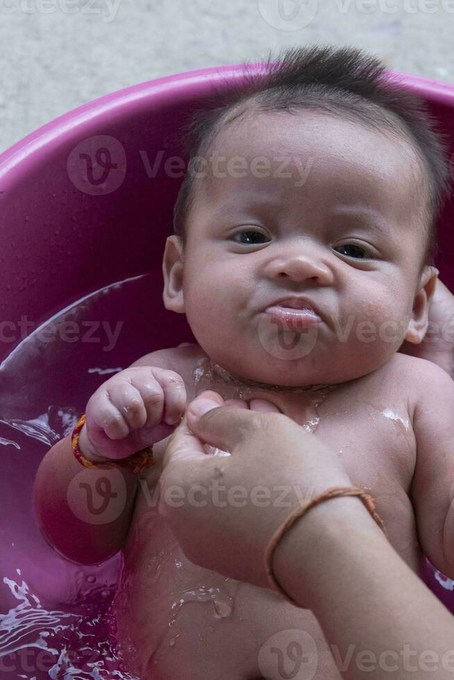 linda asiático recién nacido bebé baños en bañera madre se baña hija con calentar agua contento sonriente linda recién nacido bebé en un relajante y cómodo bañera. conceptos para cuidando para recién nacidos foto