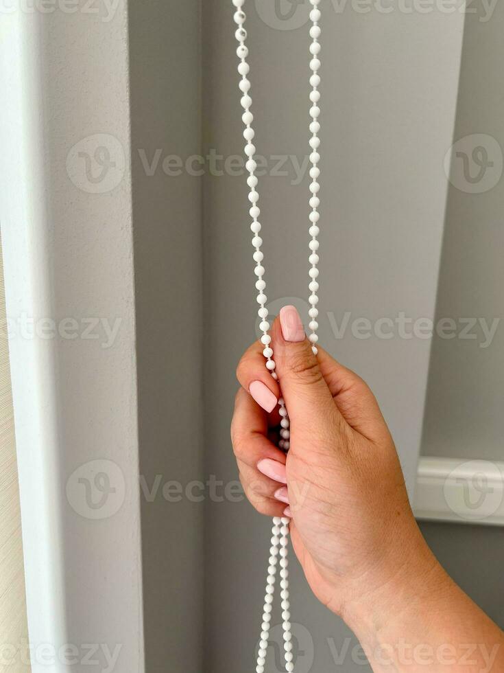 A female hand holding a beaded chain for the blinds photo