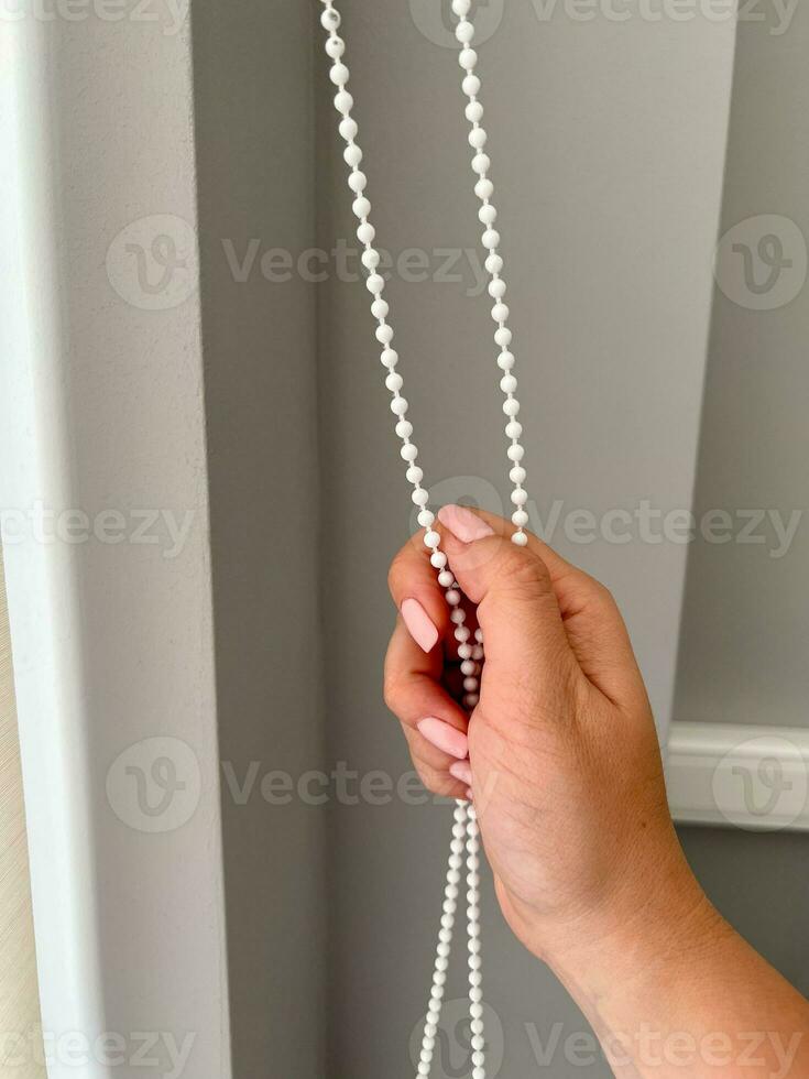 A female hand holding a beaded chain for the blinds photo