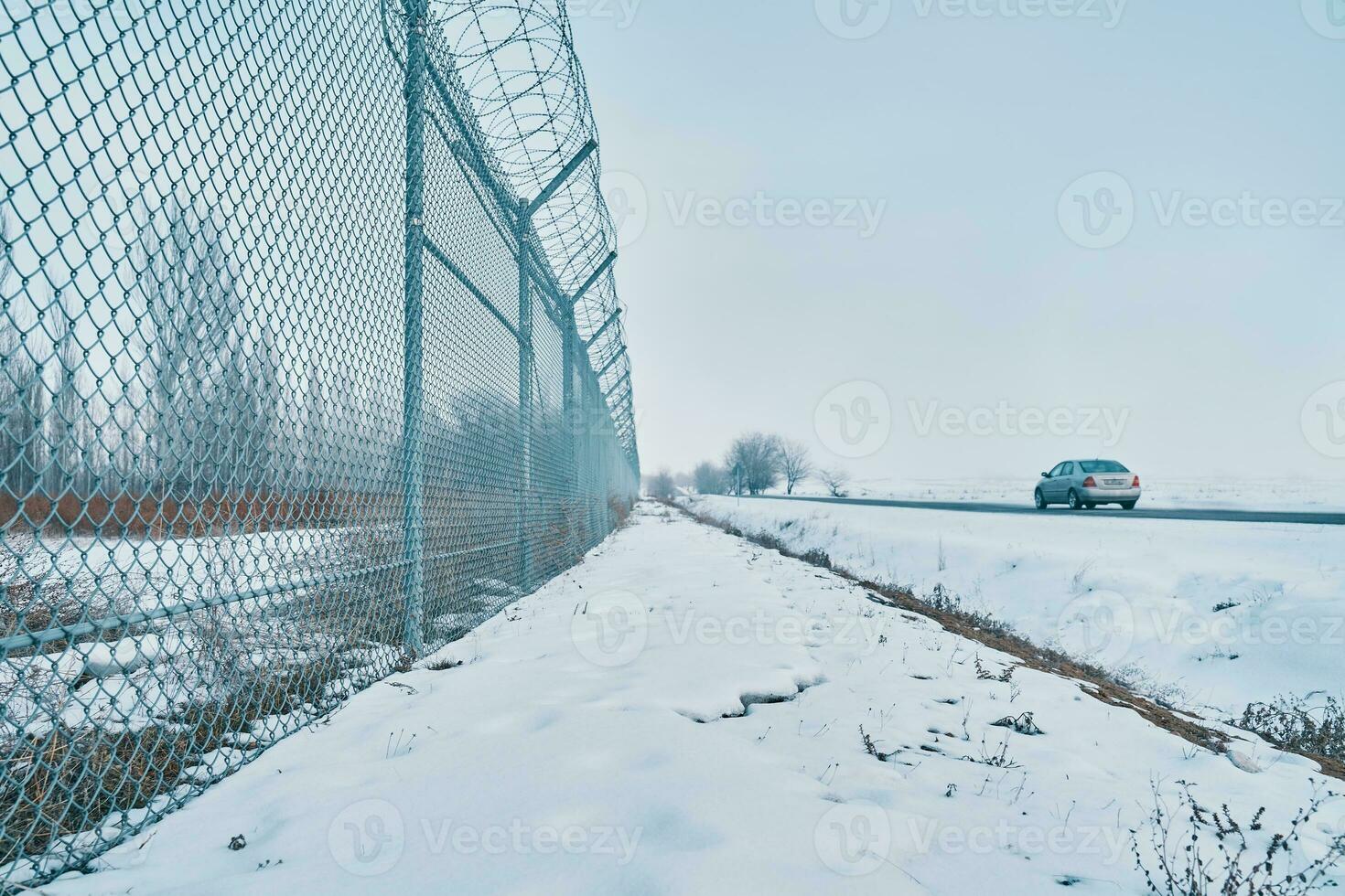 Private secured object near highway. Maximum security detention facility. Car goes on road. Barbed wire fence on border in winter. Closing for quarantine. Unauthorized entry is prohibited. photo