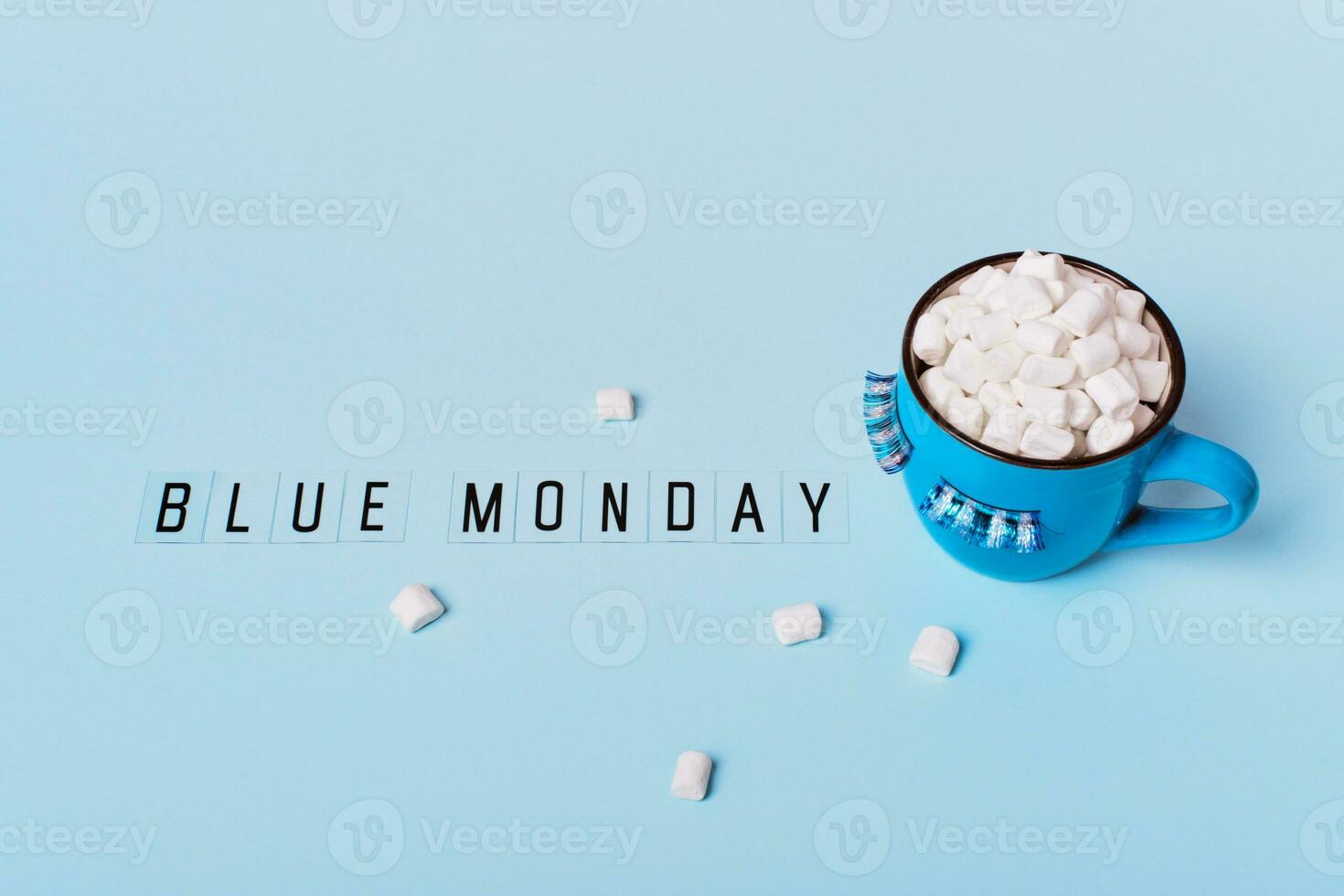 Blue monday concept. Blue monday text and mug of cocoa with marshmallows on blue background. Mug is decorated with eyelashes down photo