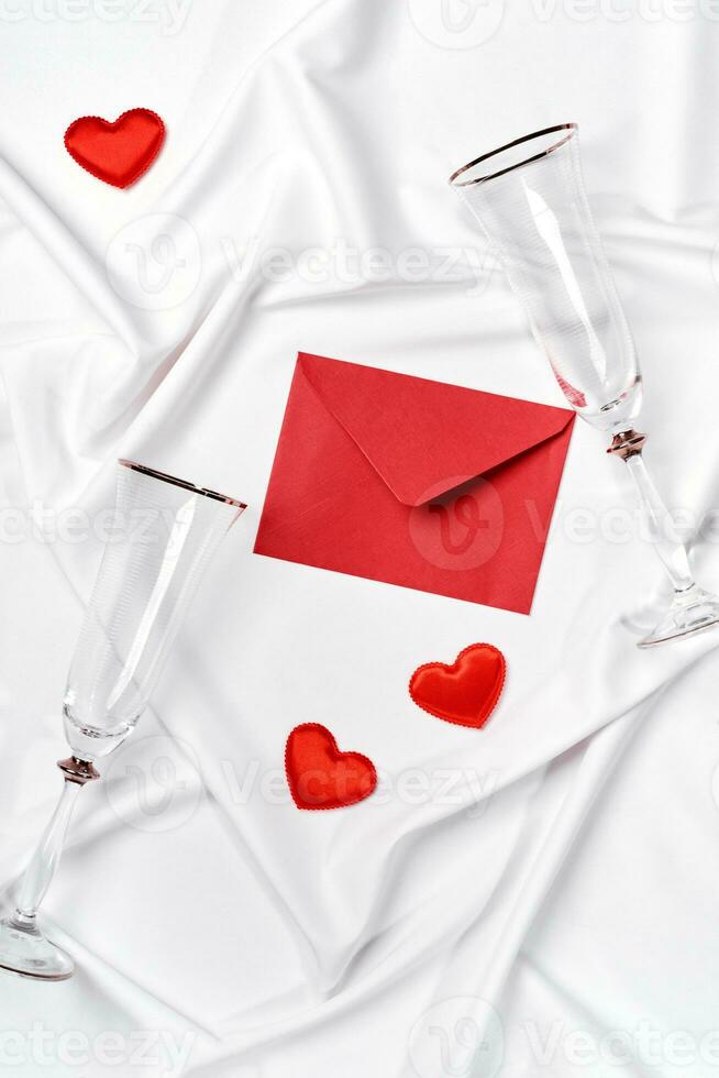 Romantic concept. Valentines day background. Red envelope, champagne glasses and hearts on white silk sheet photo