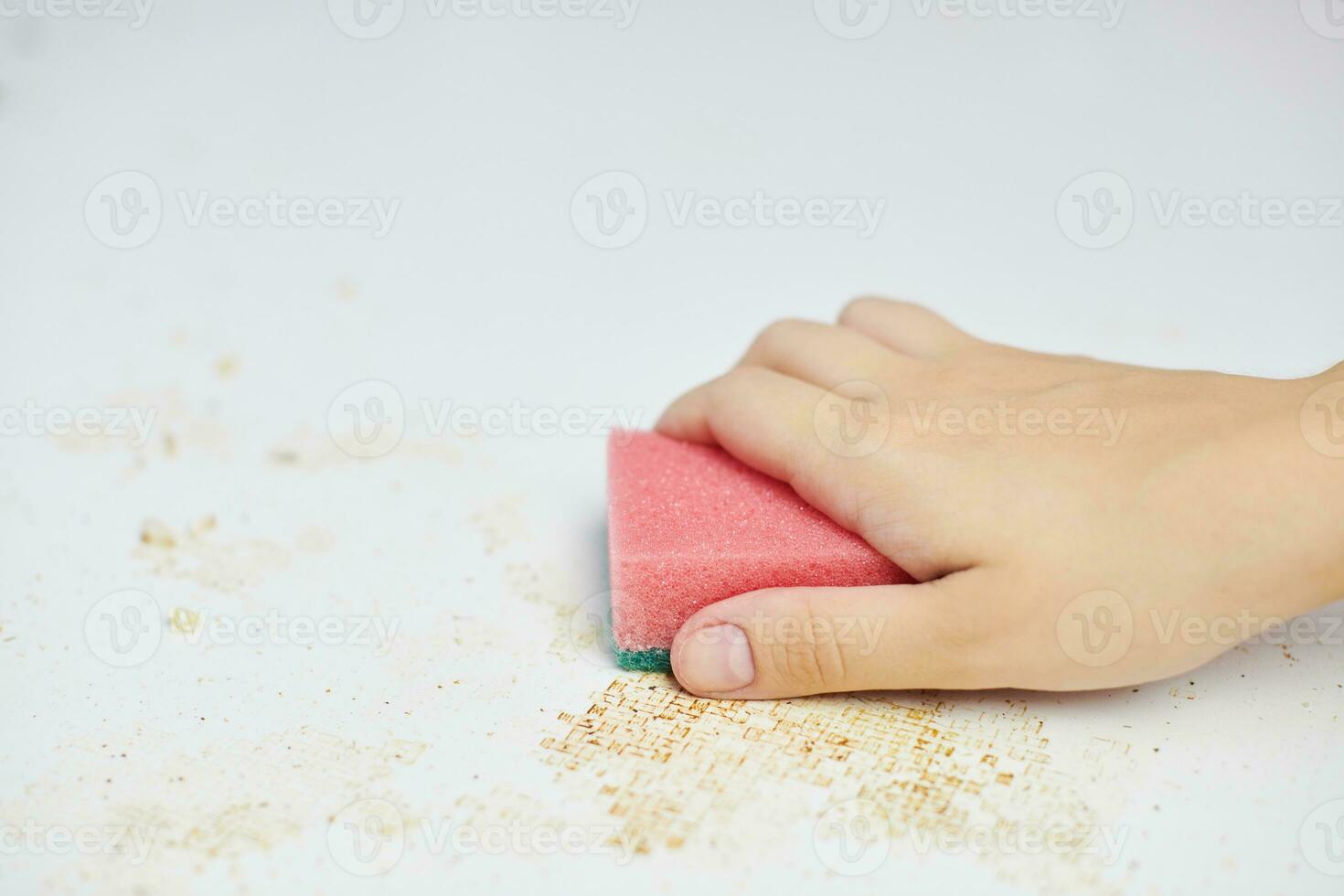 la esponja en la mano de la mujer elimina la suciedad, las migas de pan y las sobras. limpiar la mesa de la cocina. tareas del hogar foto