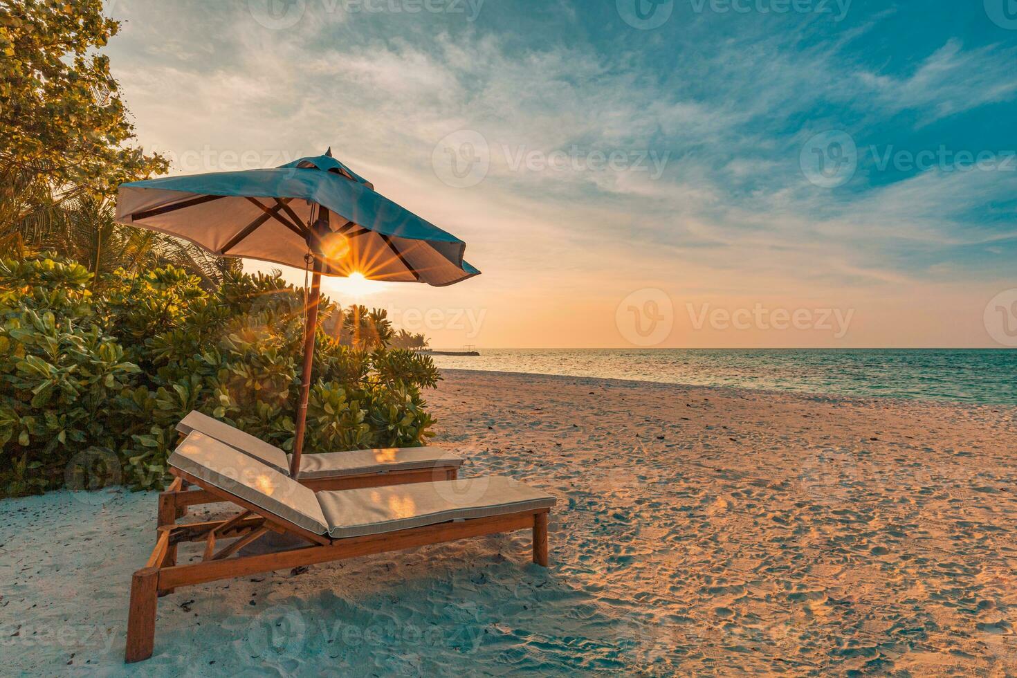 Beautiful tropical sunset scenery, two sun beds, loungers, umbrella under palm tree. White sand, sea view with horizon, colorful twilight sky, calmness and relaxation. Inspirational beach resort hotel photo