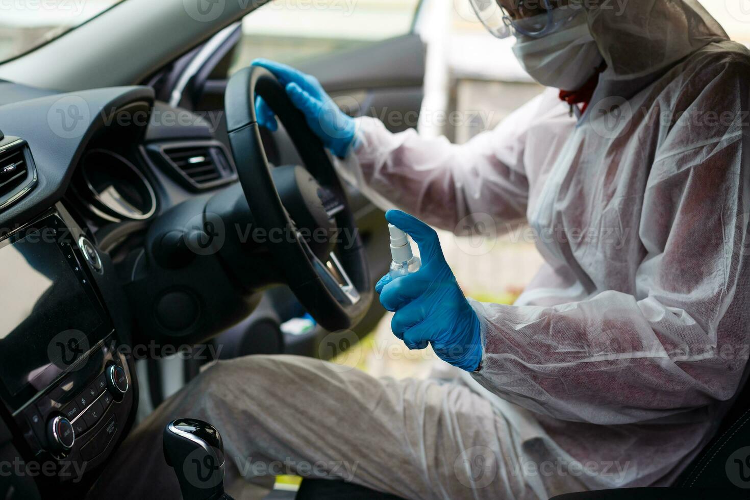 Disinfectant worker character in protective mask and suit sprays bacterial or virus in a car. photo