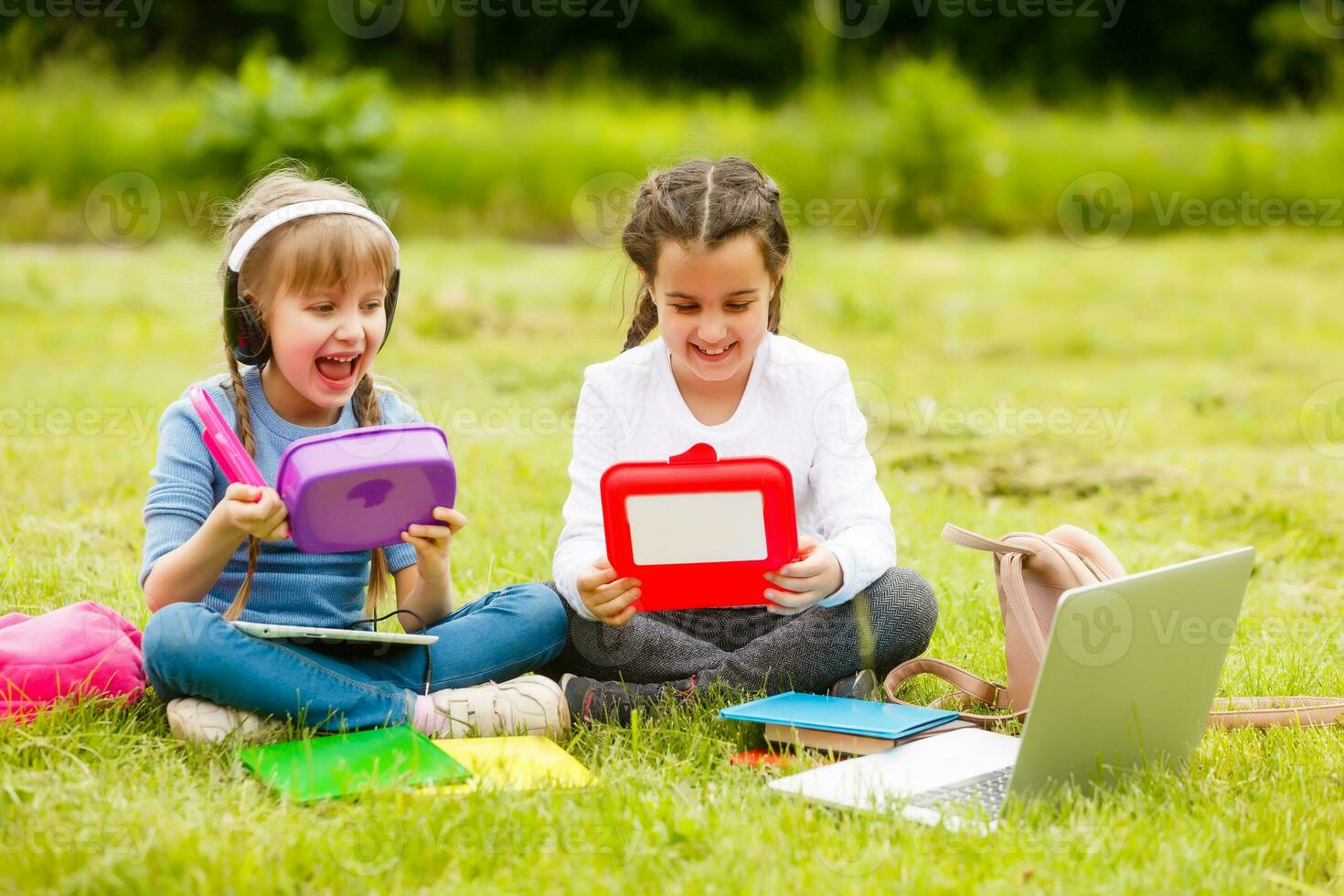 Pupils of primary school with lunch-boxes in hands. Girls with backpacks are eating on the lawn. Beginning of lessons. First day of fall. photo