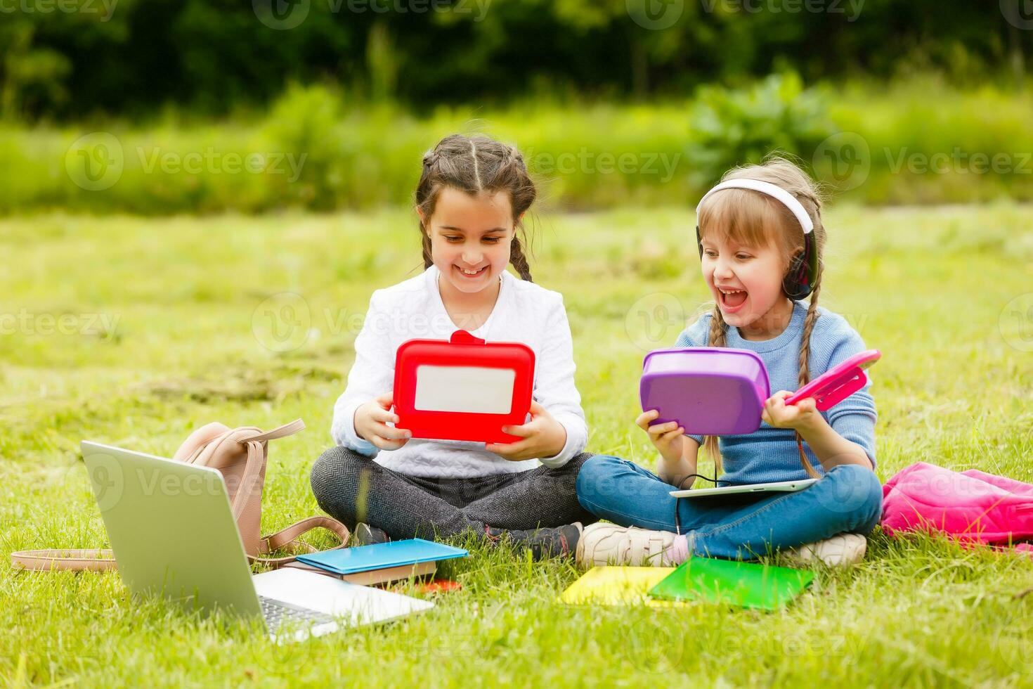 Pupils of primary school with lunch-boxes in hands. Girls with backpacks are eating on the lawn. Beginning of lessons. First day of fall. photo