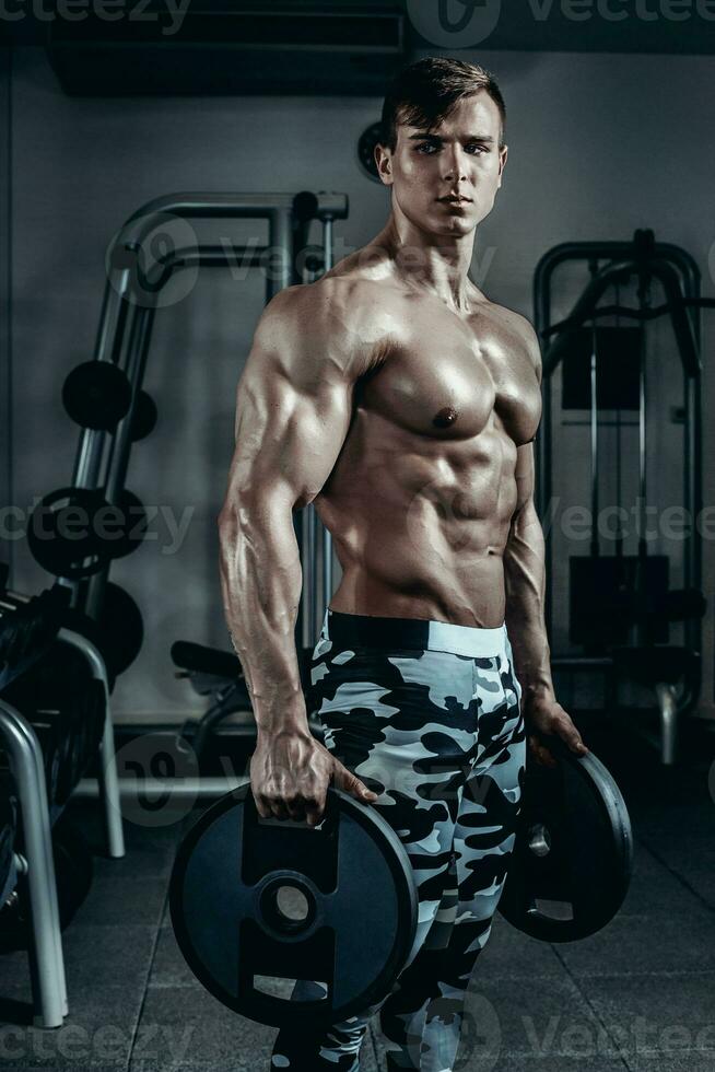 Handsome power athletic man on diet training pumping up muscles with dumbbell and barbell. Strong bodybuilder, perfect abs, shoulders, biceps, triceps and chest photo