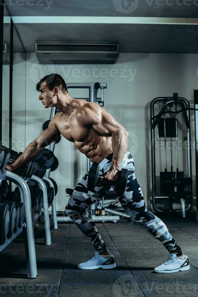Handsome power athletic man on diet training pumping up muscles with dumbbell and barbell. Strong bodybuilder, perfect abs, shoulders, biceps, triceps and chest photo