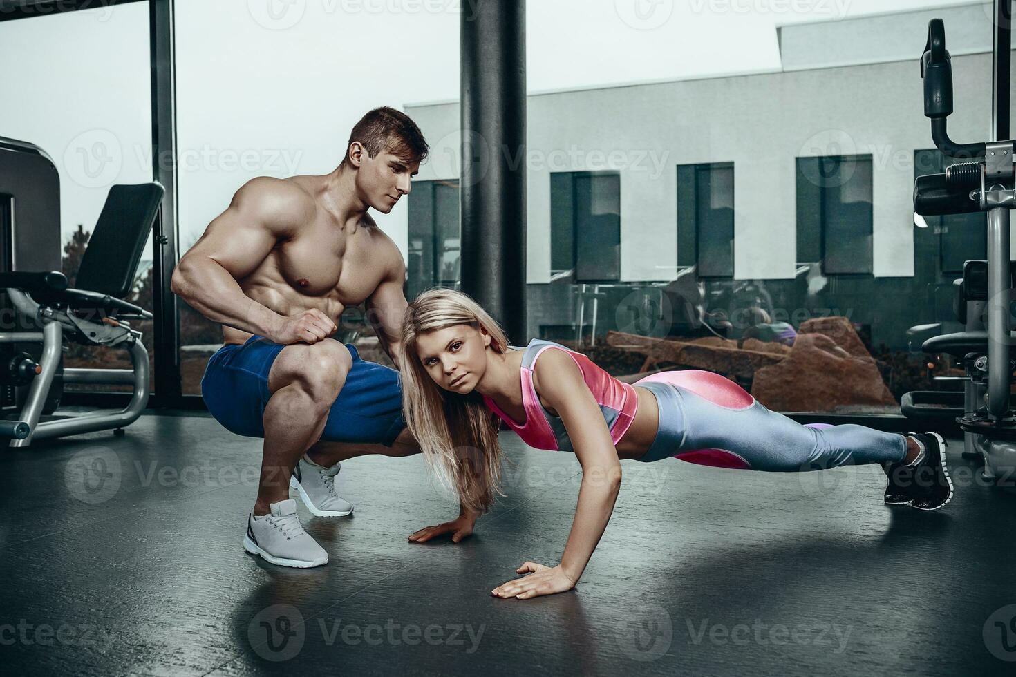 Sporty girl doing plank exercises with support of her personal trainer. photo