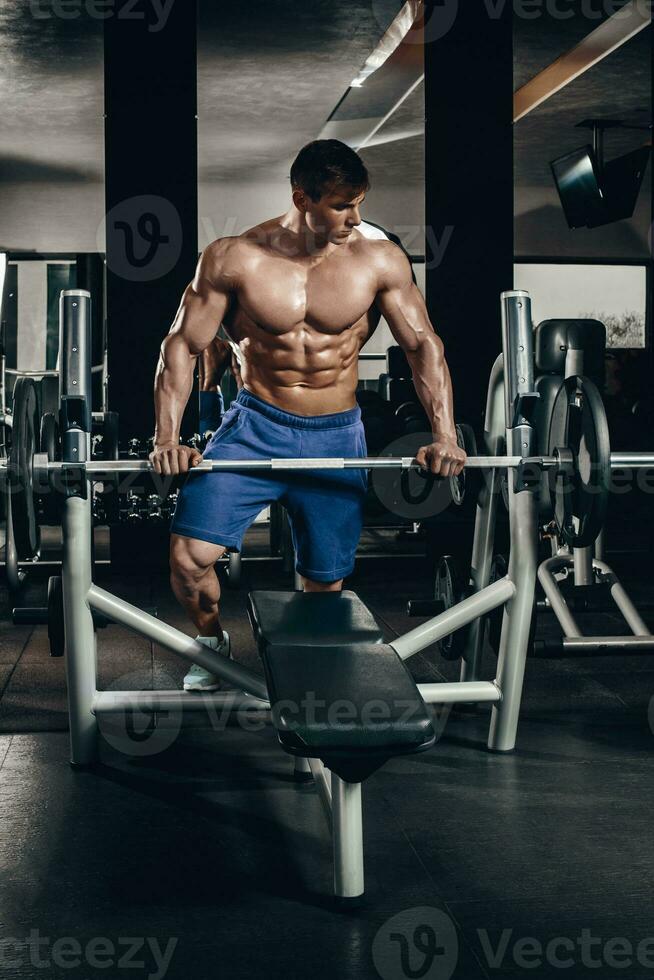 Handsome power athletic man on diet training pumping up muscles with dumbbell and barbell. Strong bodybuilder, perfect abs, shoulders, biceps, triceps and chest photo