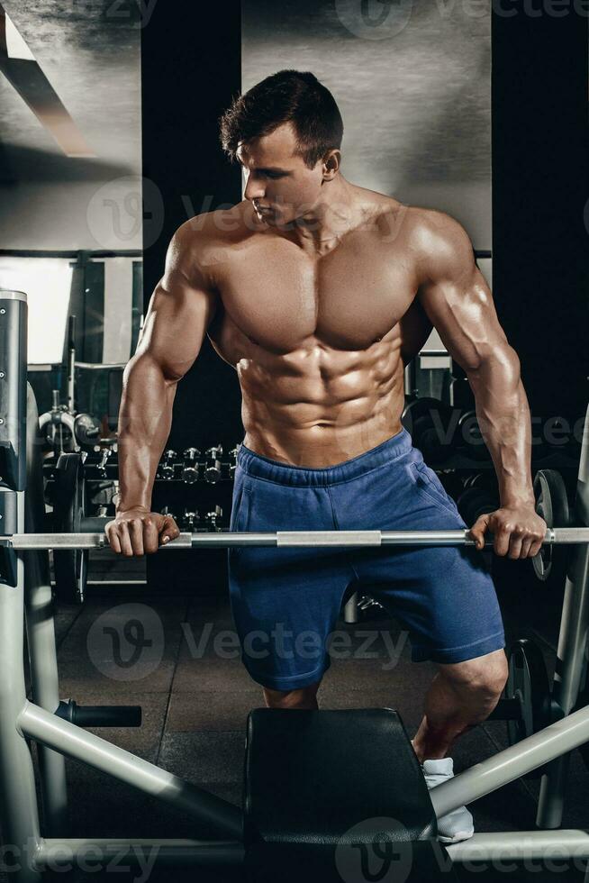 Handsome power athletic man on diet training pumping up muscles with dumbbell and barbell. Strong bodybuilder, perfect abs, shoulders, biceps, triceps and chest photo