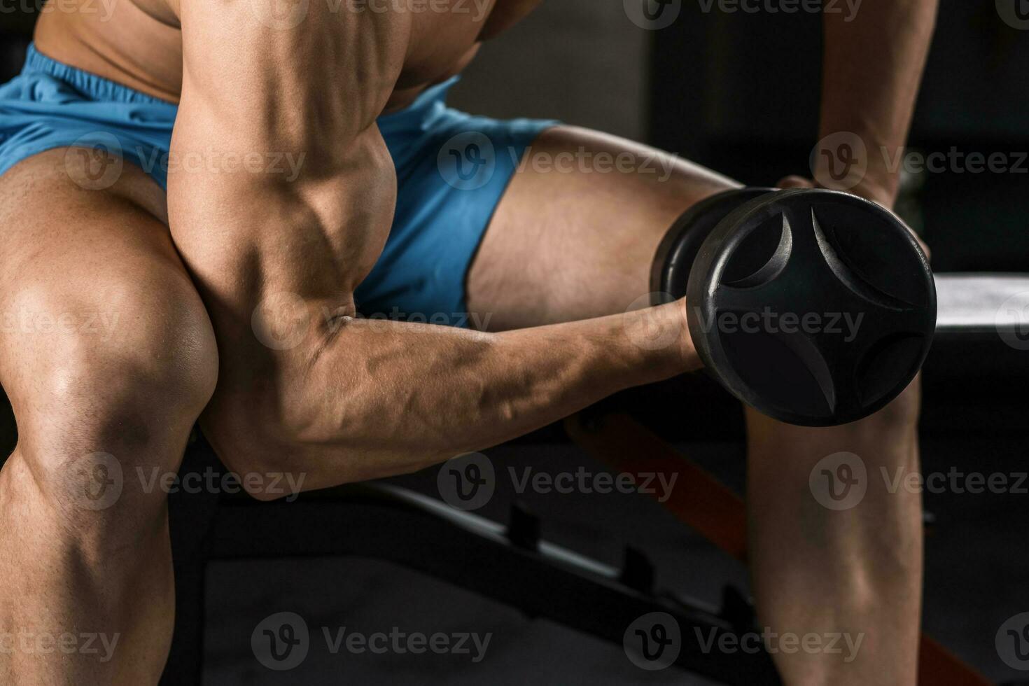 Very power athletic guy bodybuilder execute exercise with dumbbells at dark gym photo