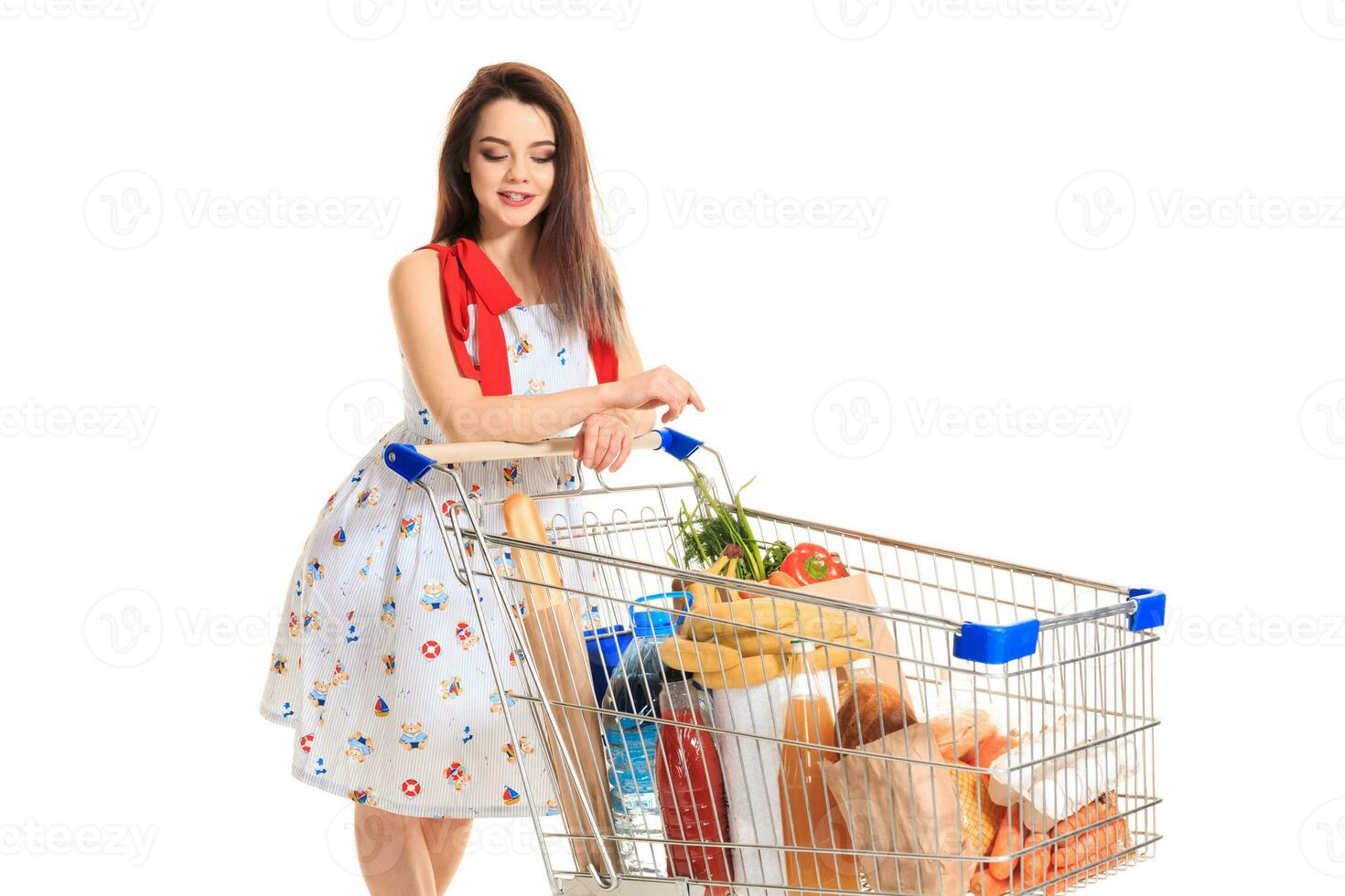 A young female pushing a shopping cart full with groceries isolated on white background photo