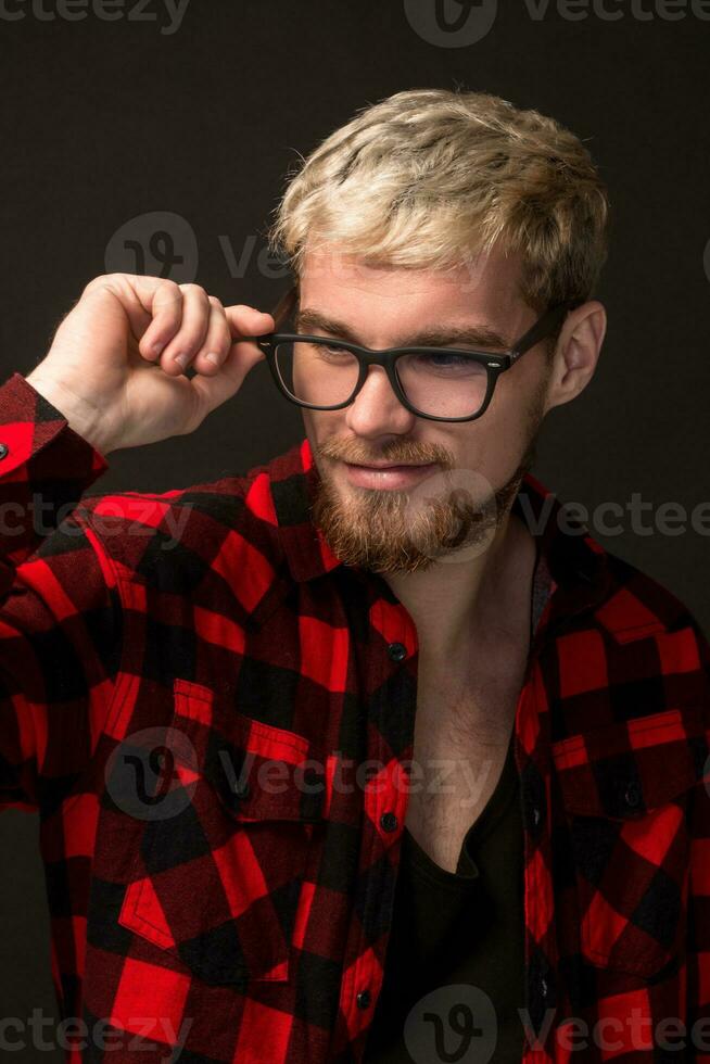Image of attractive young bearded hipster man wearing glasses dressed in shirt in a cage isolated over black background. photo