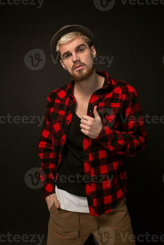 Image of attractive young bearded hipster man wearing hat dressed in shirt in a cage isolated over black background. photo