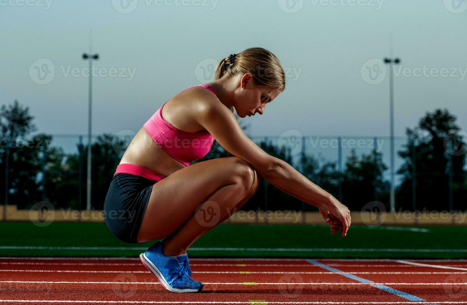 Picture of beautiful young European female runner or sprinter sitting on outdoor stadium track, feeling exhausted after sprint or marathon. photo