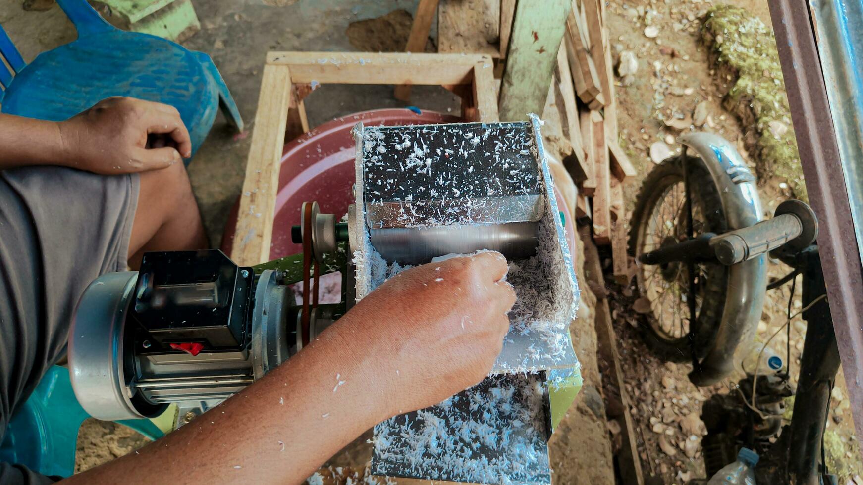 Human hands can be seen grating coconuts using a grater machine photo