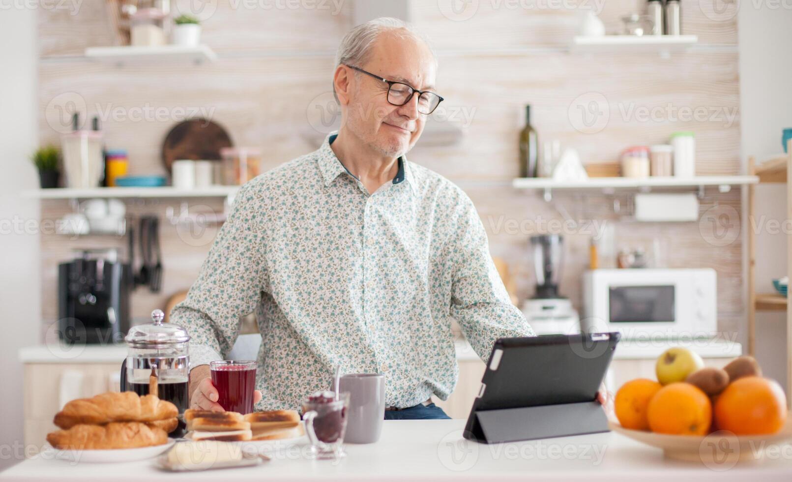 Senior person browsing on tablet pc in kitchen during breakfast having a healthy lifestyle. Elderly person with tablet portable pad PC in retirement age using mobile apps, modern internet online information technology with touchscreen photo
