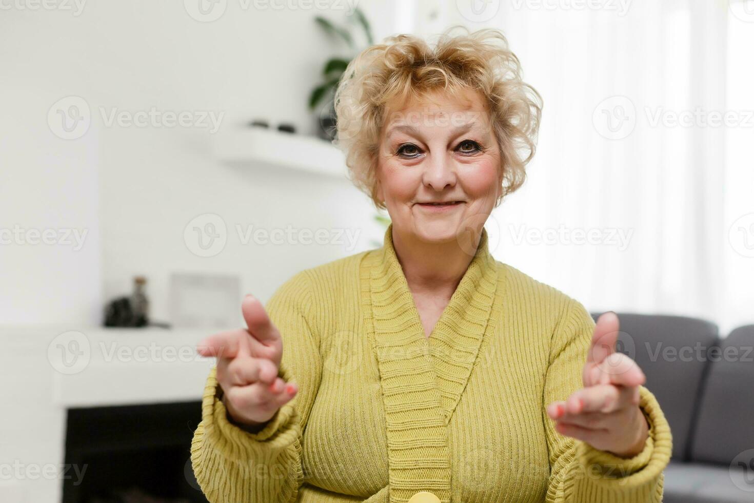 Attractive elderly woman sitting on couch at home, looking at camera, makes video call, communication distantly, modern wireless technologies concept photo