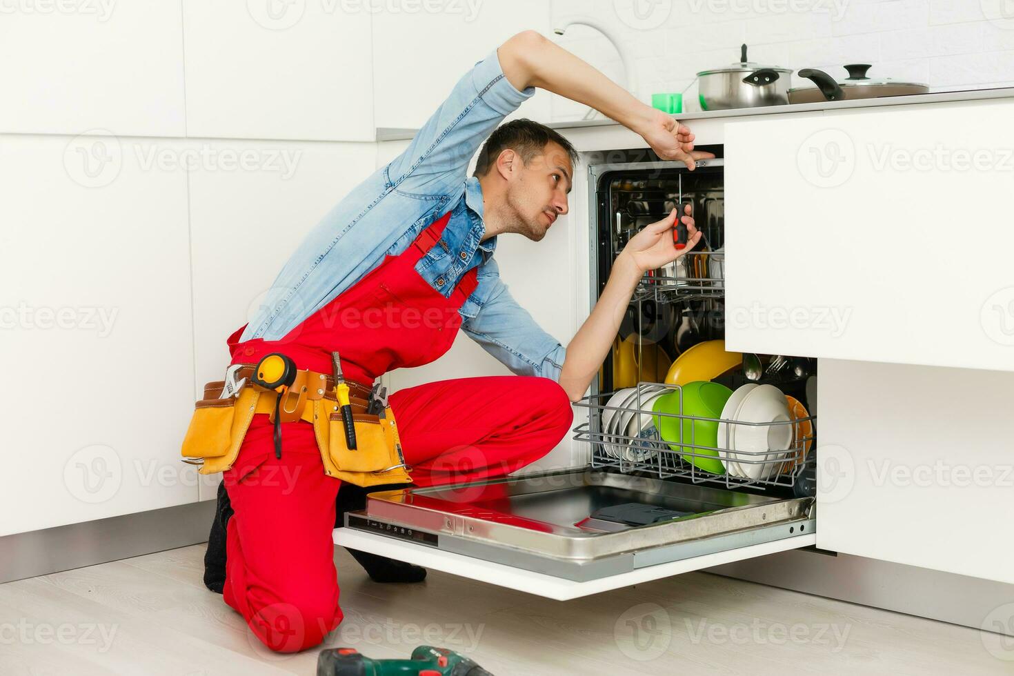 Male Technician Sitting Near Dishwasher In Kitchen photo