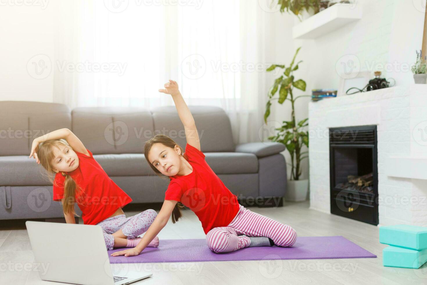two little girls practicing yoga, stretching, fitness by video on notebook. Distant online education training, aerobic at home. Healthy lifestyle, coronavirus, stay home. Kids sport home quarantine. photo