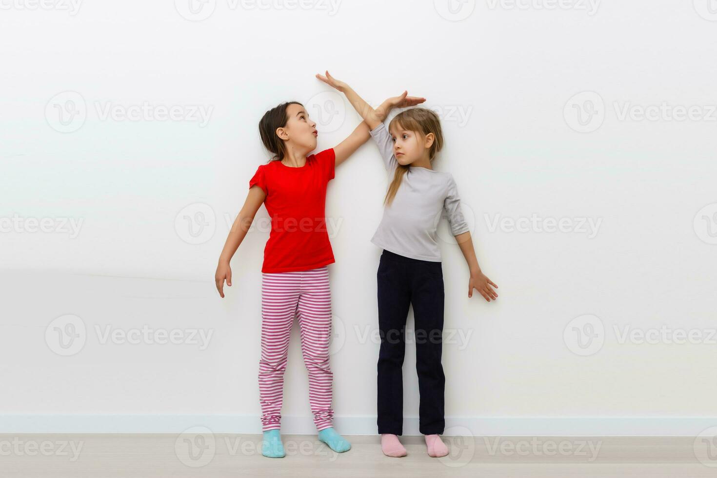 Two girls stretch up with hand on scale photo