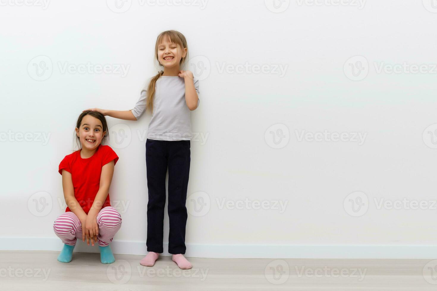 Two girls stretch up with hand on scale photo