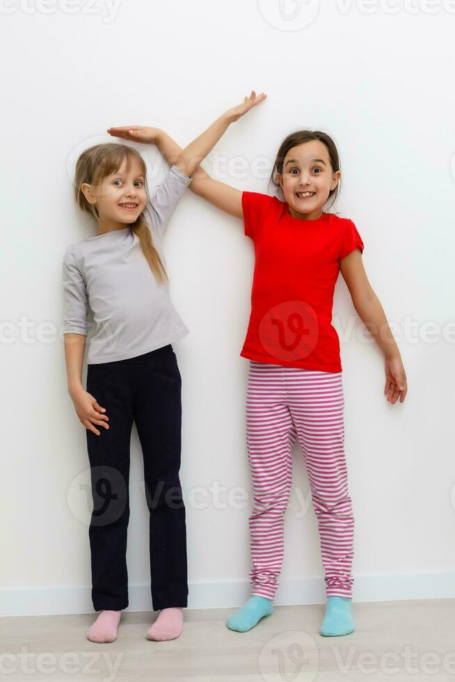 Two girls stretch up with hand on scale photo