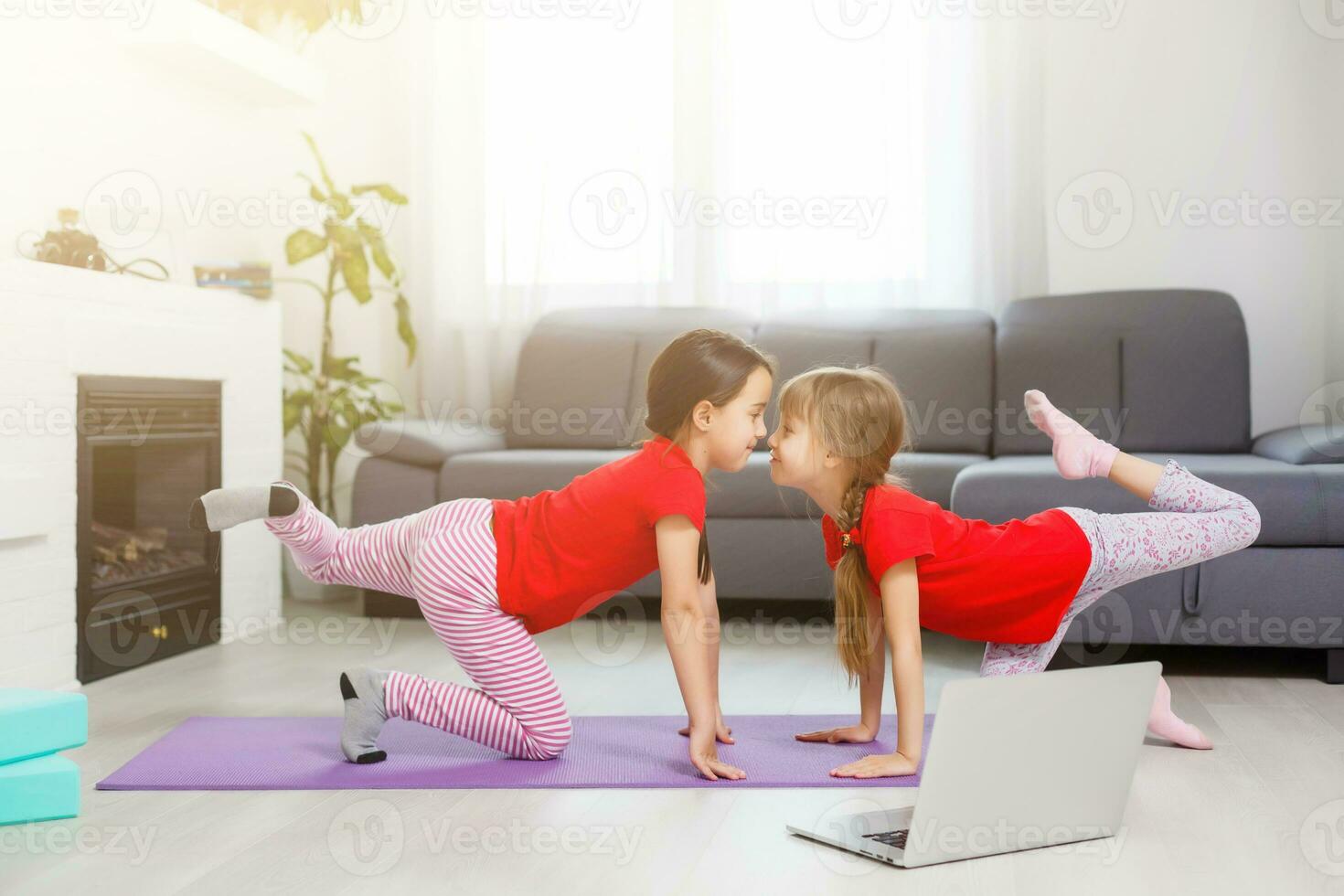 two little girls practicing yoga, stretching, fitness by video on notebook. Distant online education training, aerobic at home. Healthy lifestyle, coronavirus, stay home. Kids sport home quarantine. photo