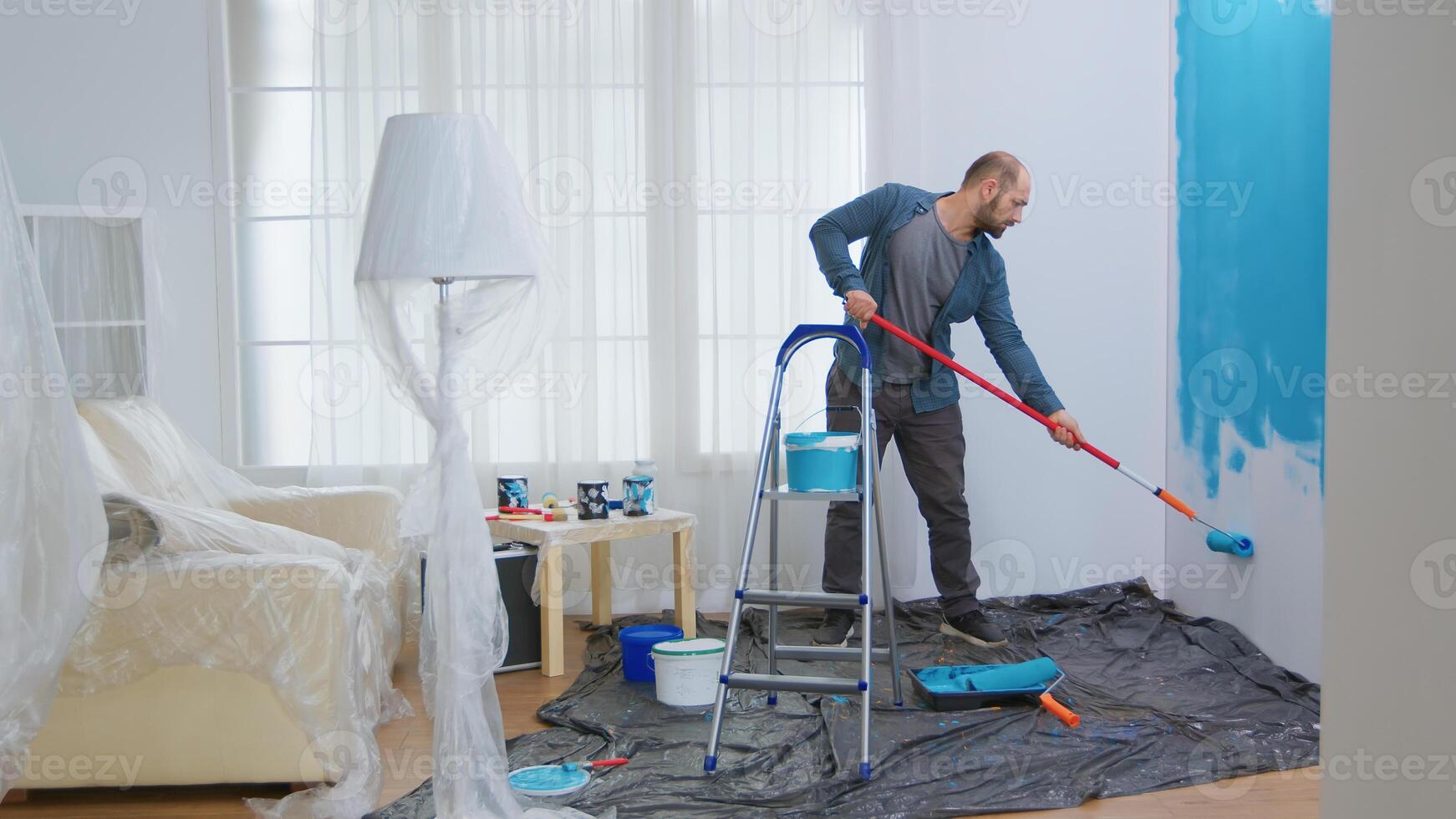 Young man painting wall with roller brush while renovating his apartment. Handyman redecoration and home construction while renovating and improving. Repair and decorating. photo