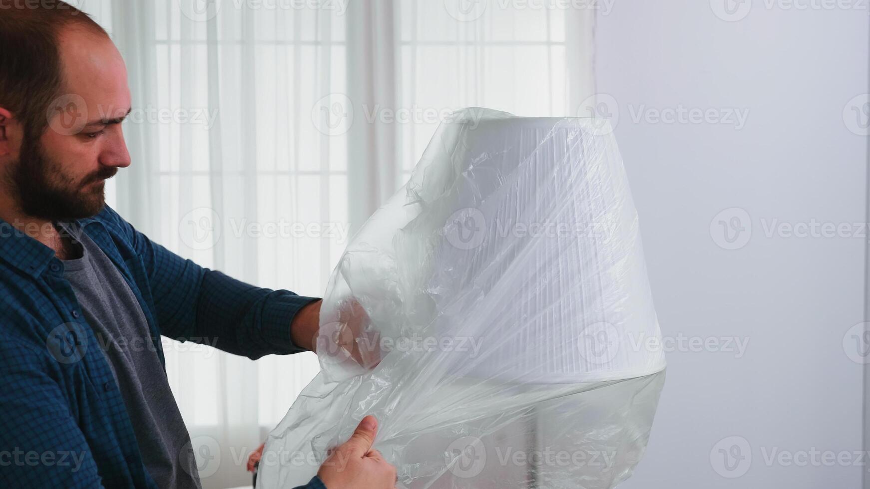 Man covering lamp with plastic sheet before home renovating. Apartment redecoration and home construction while renovating and improving. Repair and decorating. photo