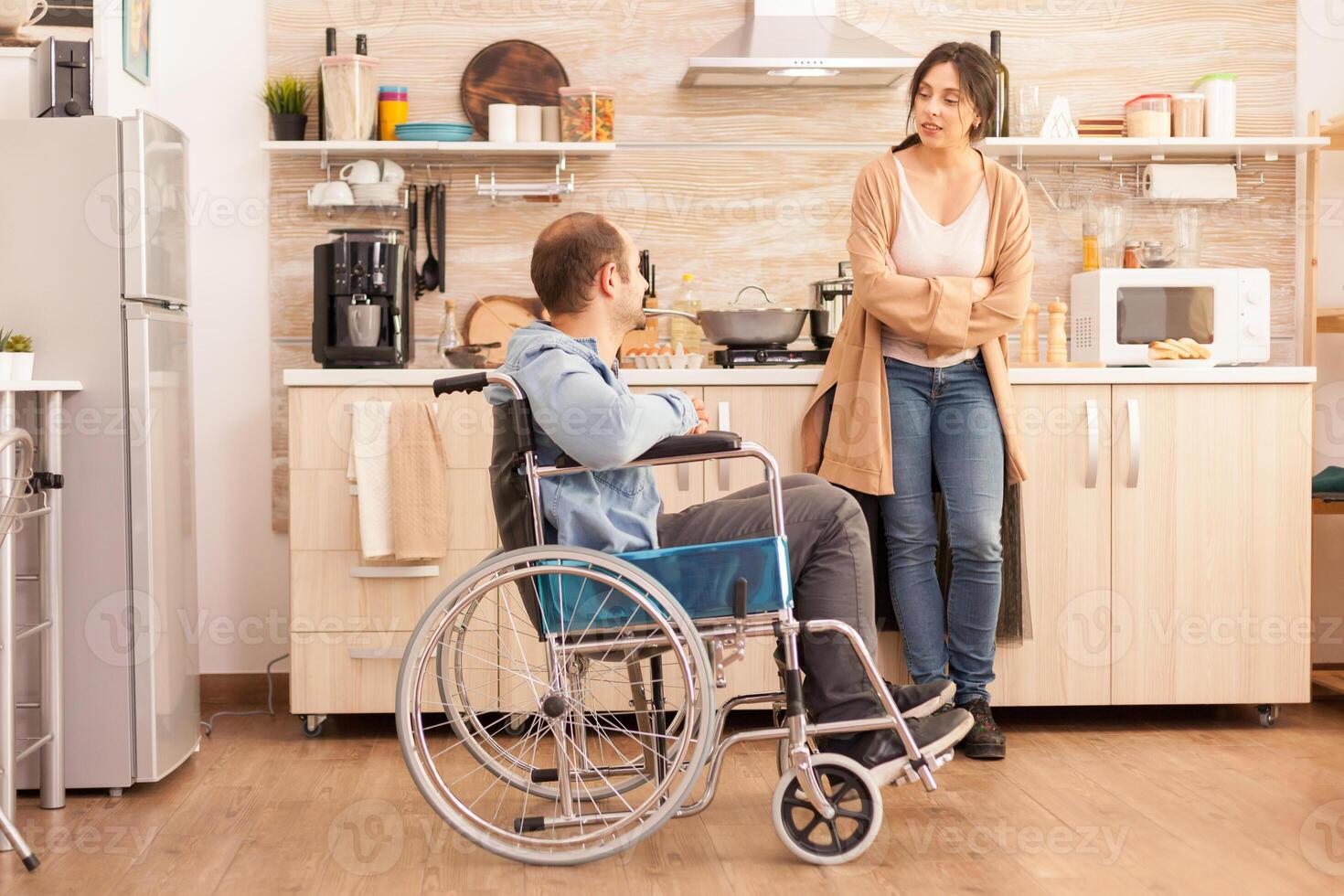 Young wife and husband with walking disability in wheelchair spending time in kitchen. Disabled paralyzed handicapped man with walking disability integrating after an accident. photo
