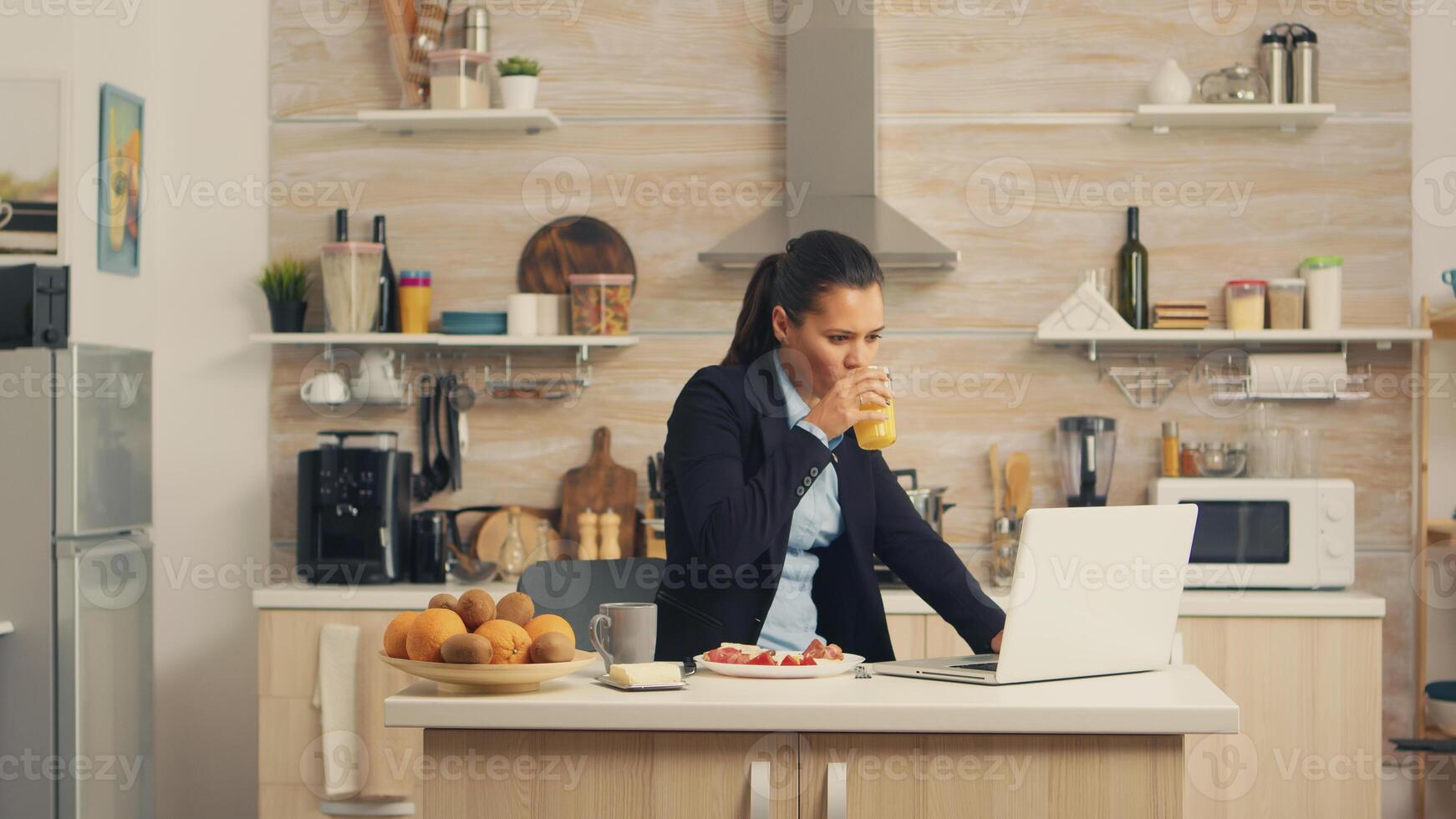 Business woman eating breakfast and working on laptop. Concentrated business woman in the morning multitasking in the kitchen before going to the office, stressful way of life, career and goals to meet photo